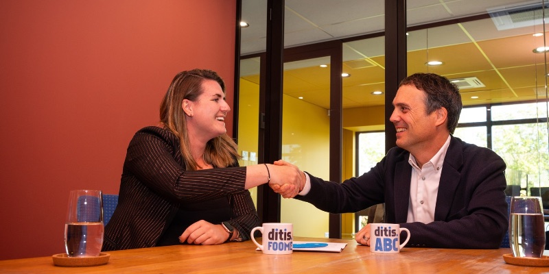 Pascale Griffioen en Michel Goulmy geven elkaar een hand, met mokken van foome en ditisABC op tafel